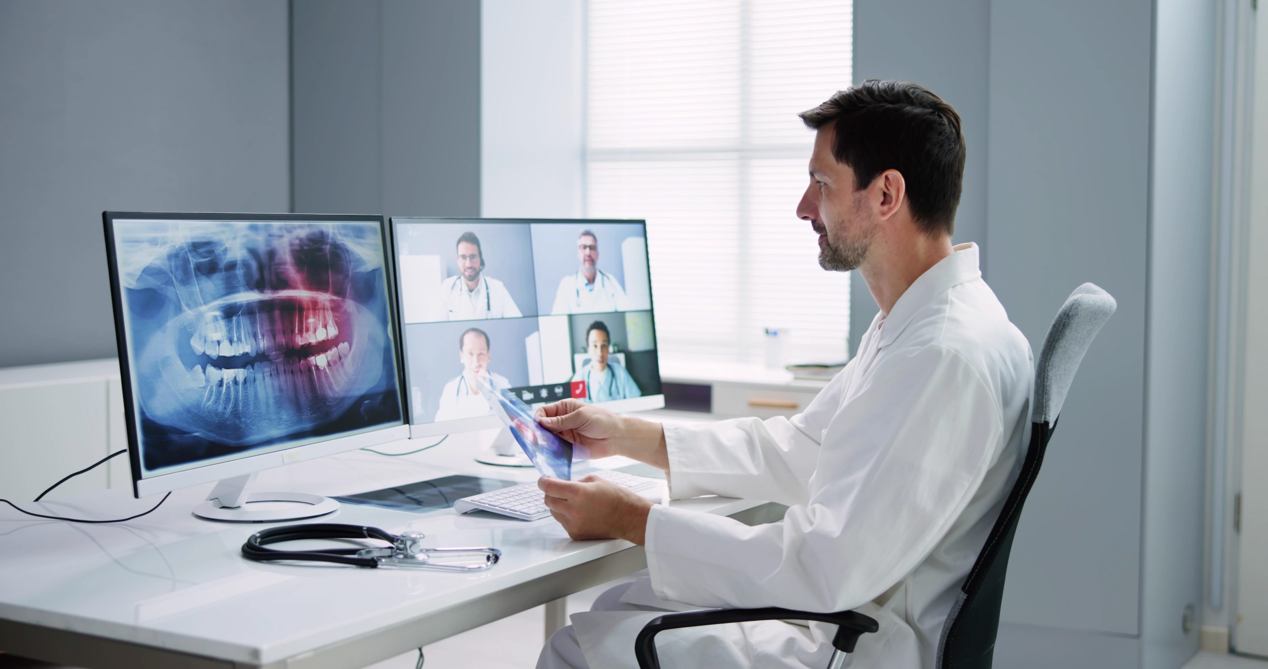 Dentist holds video conference with other dentists to discuss a patient's x-ray, illustrating a network of dentists.
