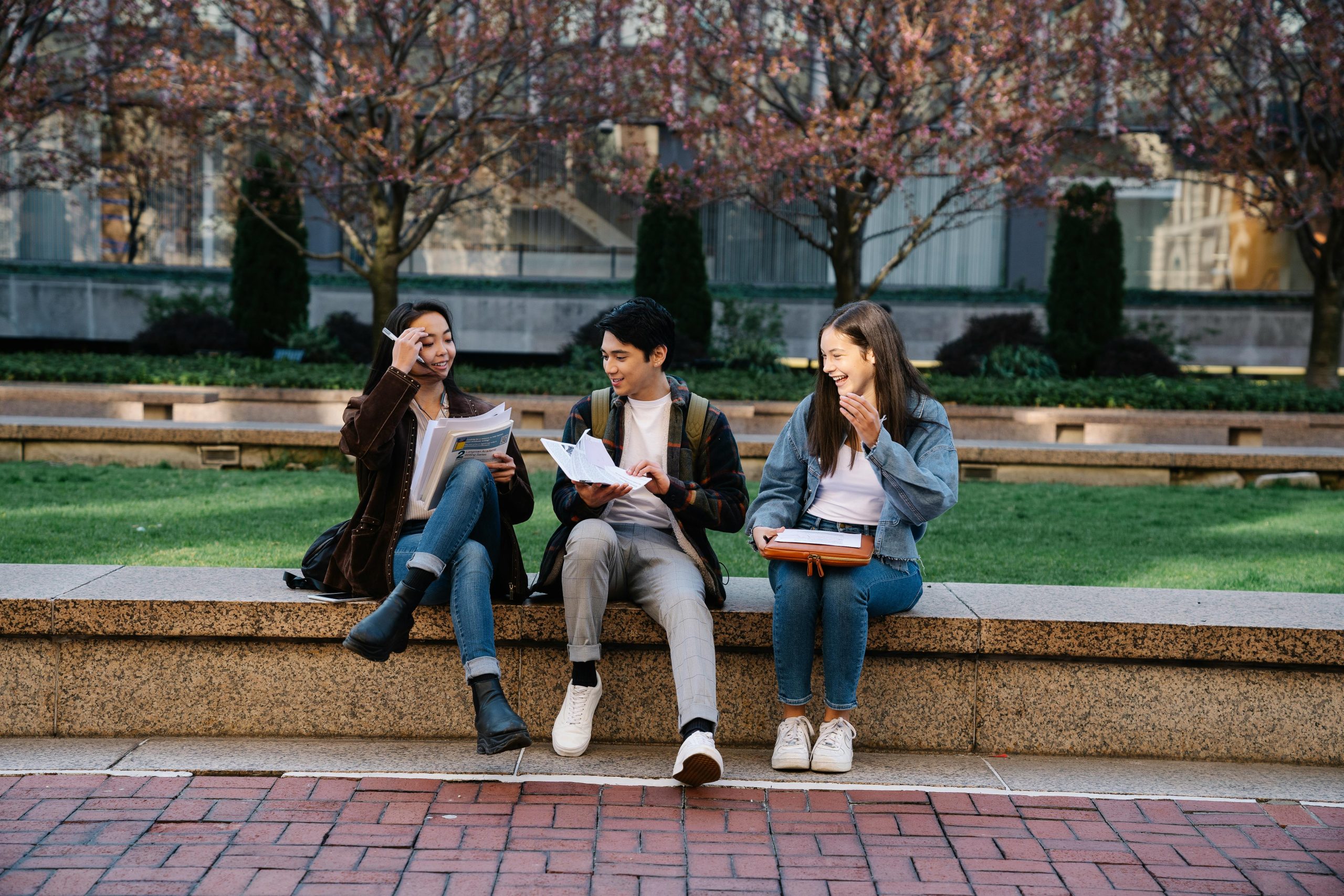 Three college students sitting outside sharing class notes.